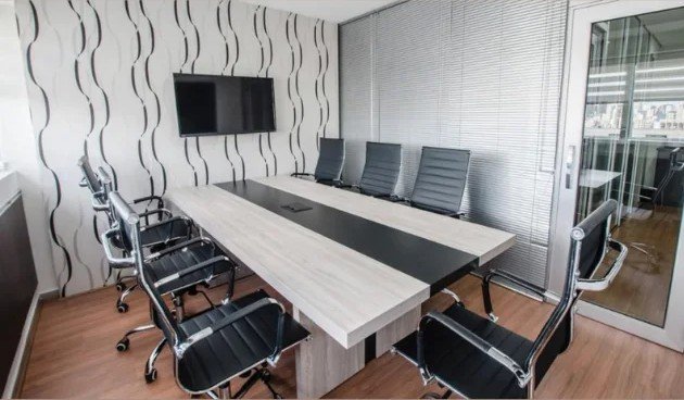 Sala de reuniões com mesa para oito lugares e televisor na parede